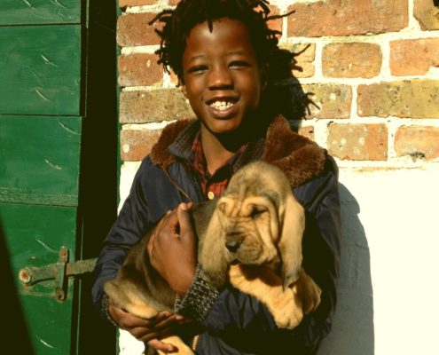 Emile houdt een pup in zijn armen naast een groene poort